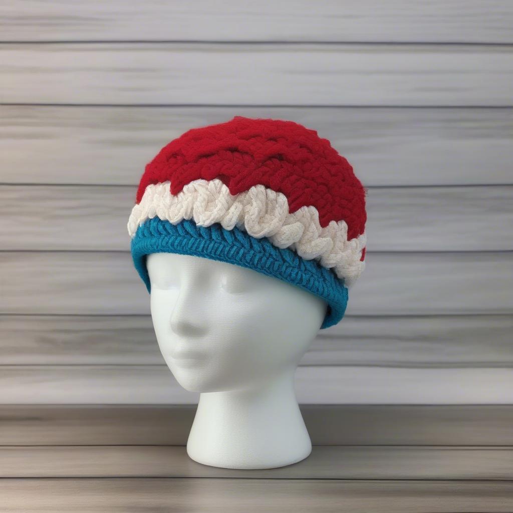 A finished crochet cupcake hat with a basket weave band and decorative "frosting" using various stitches and embellishments.