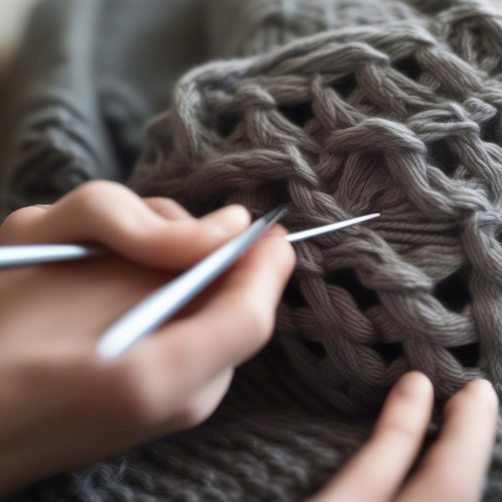 A knitter's hands working on a Celtic weave messy bun hat, showcasing the process of cabling and the use of knitting needles and yarn.