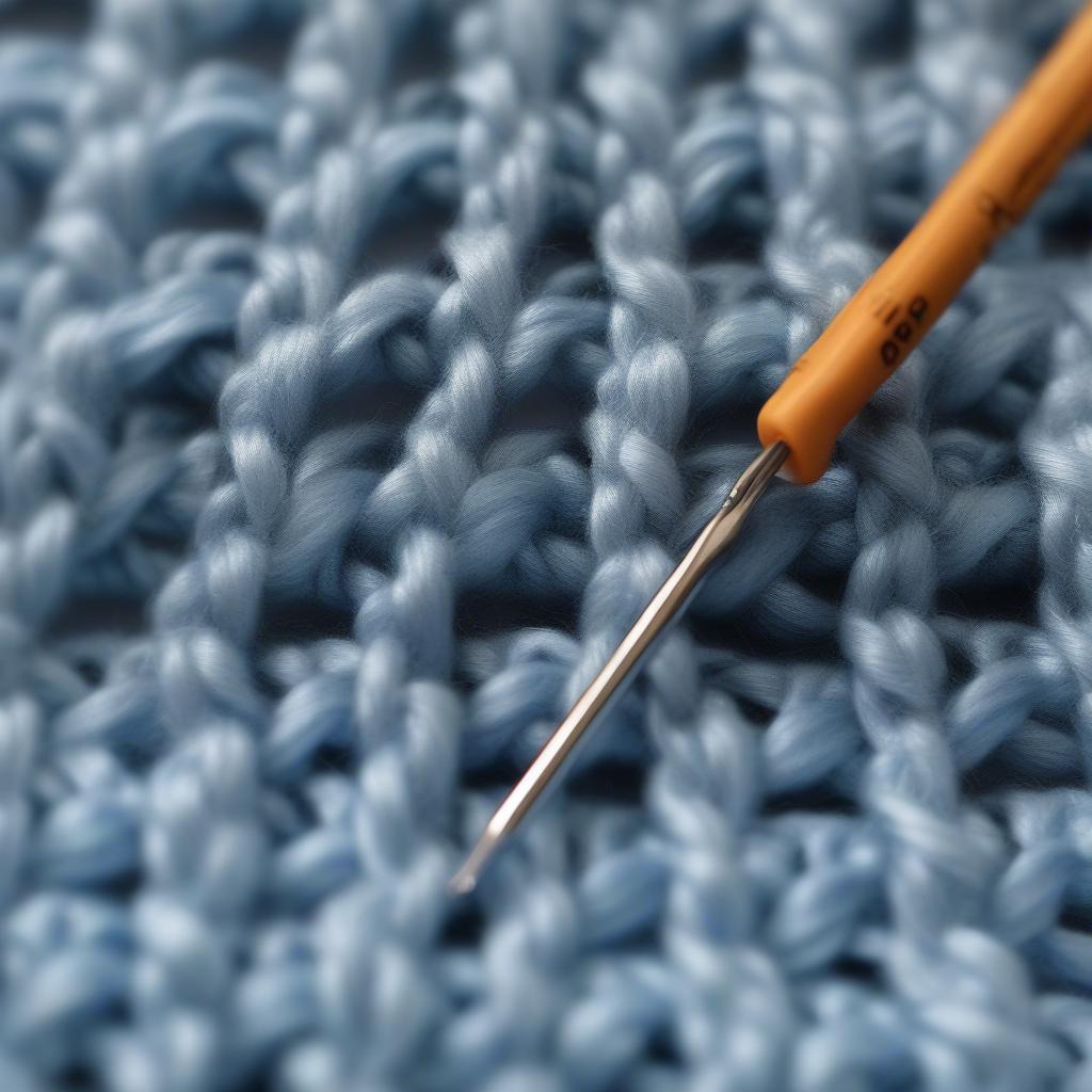 Crochet hook working on a basket weave stitch with light blue yarn, demonstrating the process.