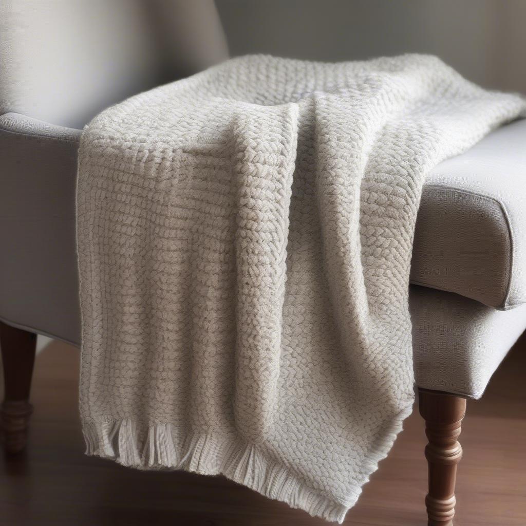 A completed basket weave knit blanket draped over a chair, showcasing the beautiful texture and pattern.